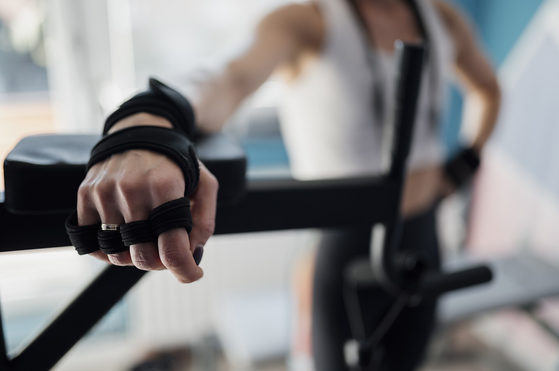 Hand mit Trainingshandschuh umgreift eine Haltestange an einem Fitnessgerät, Nahaufnahme