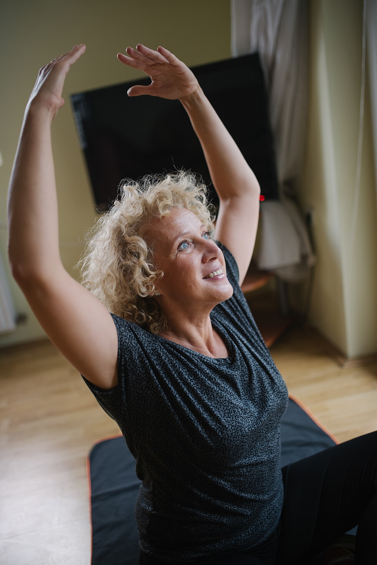 Frau streckt lächelnd beide Arme über den Kopf während einer Yoga-Einheit auf einer Matte