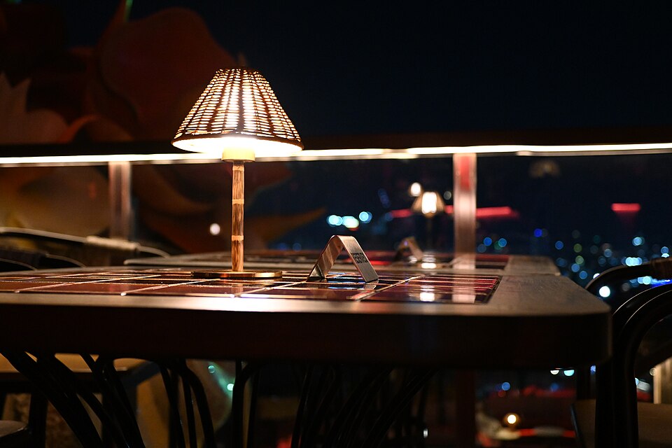Tischlampe auf einer Terrasse am Abend mit Blick über die beleuchtete Stadt