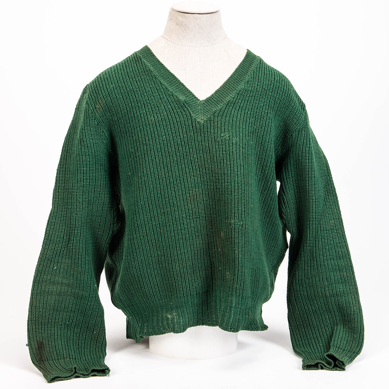 Tannengrüner Pullover aus Rippstrick mit V-Ausschnitt auf einer Leinen-Schneiderpuppe vor hellem Hintergrund